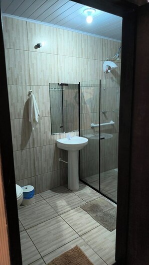 A bathroom with a glass shower enclosure, a white sink, and a mirror above it. - Pousada Cantinho da Jake (Penha)