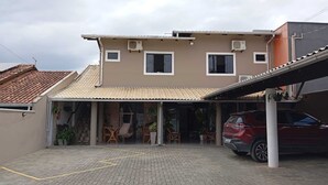 A two-story building with a tiled roof, a covered entrance, and a parked red SUV. - Pousada Cantinho da Jake (Penha)