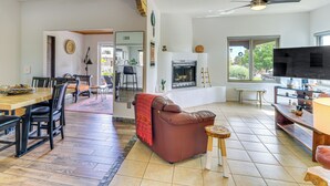 Uma sala de estar ampla com lareira, um espaço de jantar com mesa e cadeiras de madeira, e uma televisão sobre um suporte de madeira.