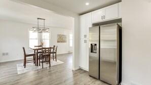 A modern kitchen with white cabinetry, a stainless steel refrigerator, and a dining area with wooden chairs and a table. - Walk to River, Parks & Dining: Family Home w/ Yard (National Park)