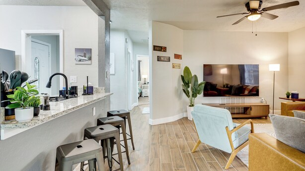 Une cuisine moderne avec un comptoir en marbre, des tabourets de bar et un coin repas comprenant une chaise bleu clair et une table en bois.