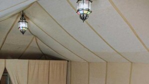 A tent-style bedroom with a bed, pillows, and a nightstand. - Unique Sahara Camp (Merzouga)