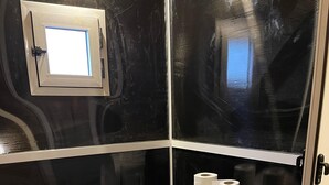 A small, enclosed bathroom with a toilet, a trash bin, and a window. - Unique Sahara Camp (Merzouga)