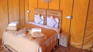A tent-style room with a bed, pillows, a small table, and a hanging light fixture. - Unique Sahara Camp (Merzouga)