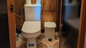 A compact bathroom with a toilet, a trash bin, and a toilet paper holder. - Unique Sahara Camp (Merzouga)