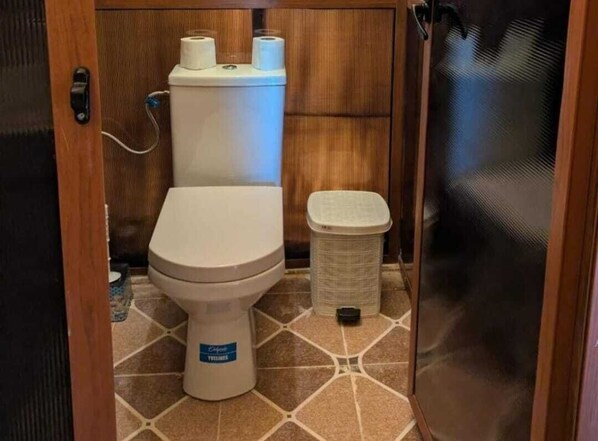 Un baño pequeño con inodoro, un cesto de basura y un dispensador de papel higiénico.