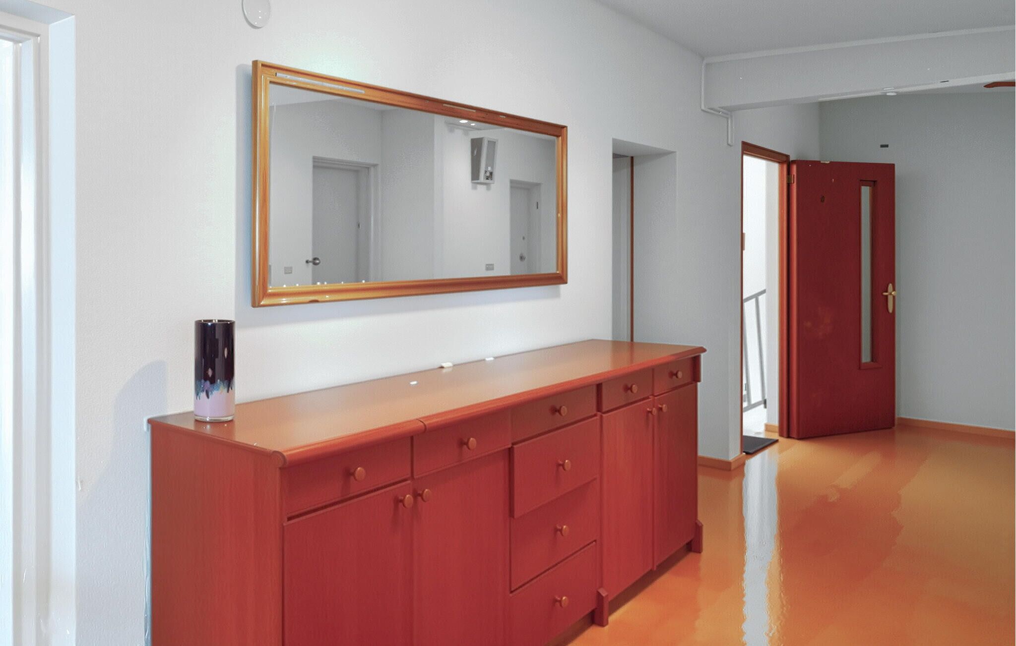 Una habitación con un aparador de madera, un espejo grande y una puerta roja.