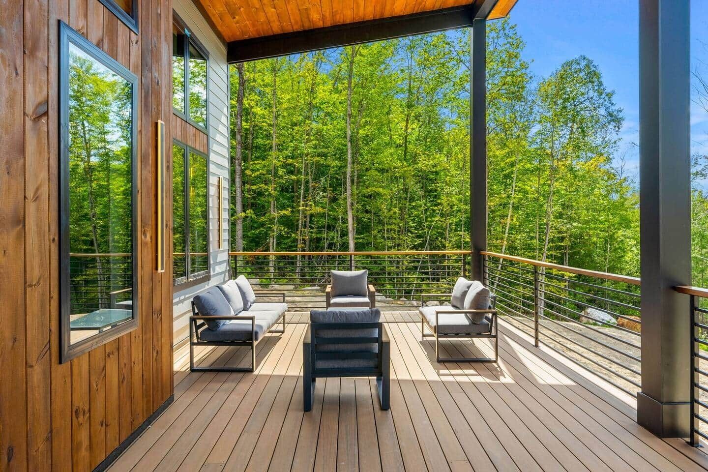 Une terrasse en bois avec des sièges d’extérieur et une vue sur une forêt.