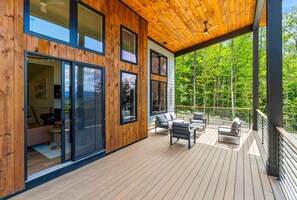 A modern wooden deck with outdoor furniture, large windows, and a view of a forest. - Luxury Mountain Estate, Sleeps 12, Theater, Games & Hot Tub (Campton)