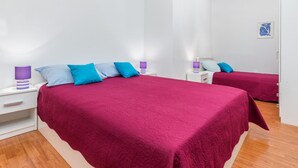 Un dormitorio con dos camas, cada una con una colcha roja y varios almohadones. Hay dos mesitas de noche con lámparas y un pequeño cuadro en la pared.