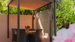 Un patio al aire libre con una mesa y sillas, una planta en maceta y una valla de bambú.
