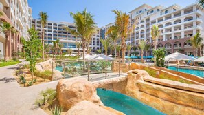 Ein Resort mit mehreren Gebäuden, einem zentralen Poolbereich mit Felsformationen und Palmen.