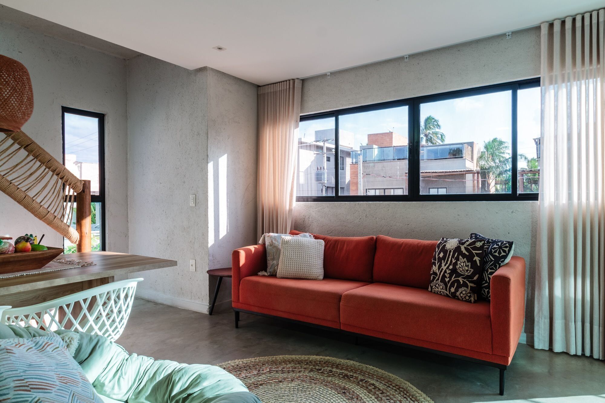 A modern living room with a red sofa, a wooden coffee table, and a large window with curtains.