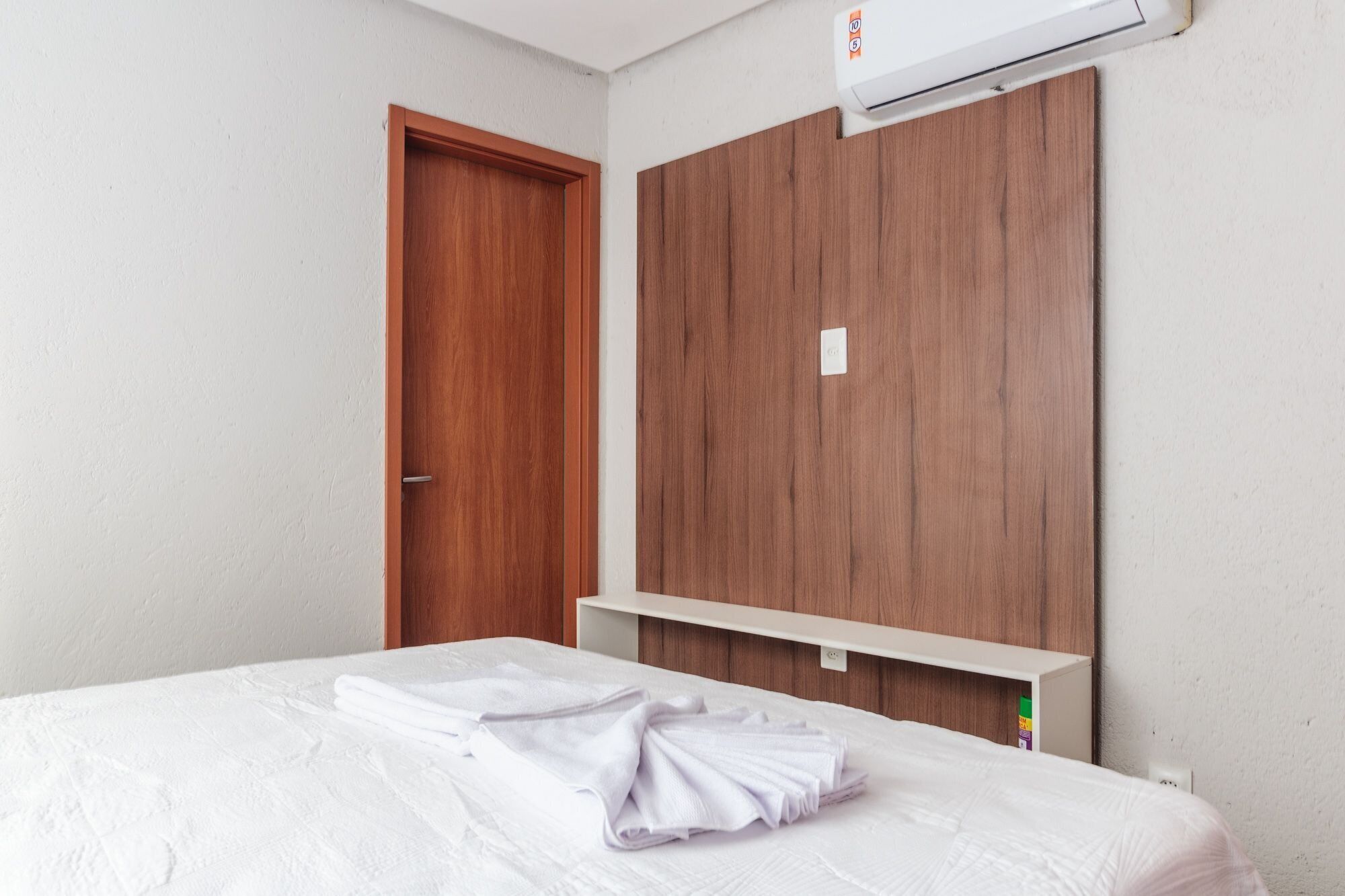 Een slaapkamer met een houten garderobe, een bed met witte lakens en een witte airconditioning op de muur.
