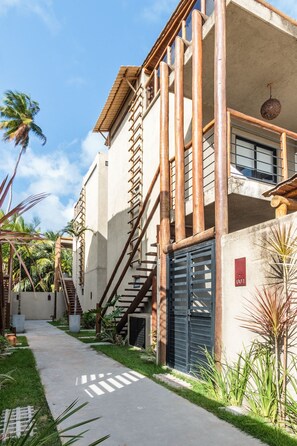 A building with a concrete facade, wooden staircases, and a black gate. - MHV Milagres - Lanai House 18 (São Miguel dos Milagres)