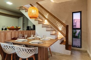 Un coin repas avec une table en bois dressée pour quatre personnes, un escalier en osier et une vue par la fenêtre.