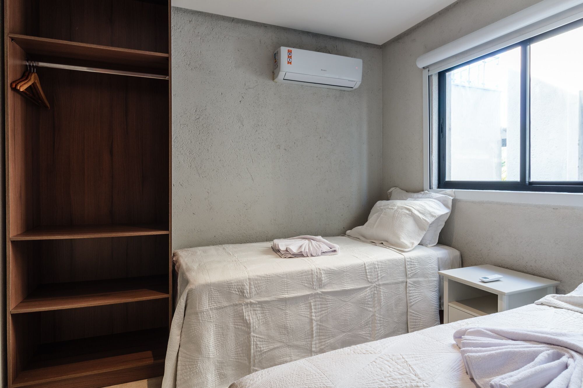 Ein Schlafzimmer mit Holzschrank, einem Einzelbett mit weißer Decke, einem kleinen Nachttisch und einem Fenster mit Blick.