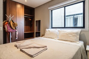 Une chambre à coucher avec un lit, une fenêtre, une armoire et un porte-manteau avec des chapeaux et des sacs.