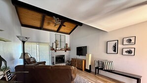 Un salon avec un canapé marron, une table basse, une cheminée, un téléviseur et un ventilateur de plafond.