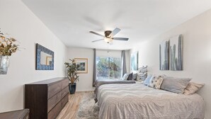 Une chambre à coucher comprenant un lit, une commode, un ventilateur de plafond et des œuvres d’art accrochées aux murs.