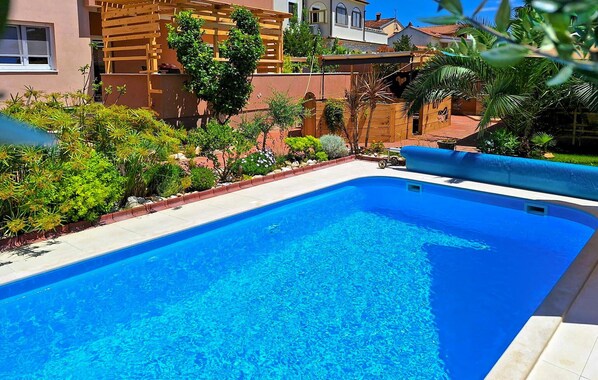 A swimming pool with a wooden deck and surrounding greenery. - Gorgeous apartment in Medulin (Medulin)