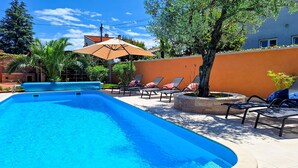 A swimming pool with lounge chairs and an umbrella, surrounded by a low wall and trees. - Gorgeous apartment in Medulin (Medulin)