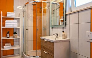 A modern bathroom with a glass shower enclosure, a vanity with a mirror, and shelves with towels. - Gorgeous apartment in Medulin (Medulin)