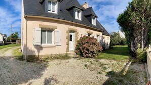 A two-story house with a gravel driveway, a stone wall, and a large bush with pink flowers. - Family home near the beach, enclosed garden, 4 bedrooms, sleeps 10 (Loctudy)