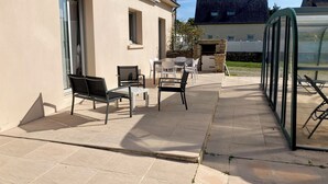 A patio area with outdoor furniture, a stone fireplace, and a glass enclosure. - Family home near the beach, enclosed garden, 4 bedrooms, sleeps 10 (Loctudy)