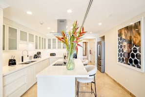 A modern kitchen with white cabinetry, a central island, a vase with flowers, and a large abstract painting on the wall.