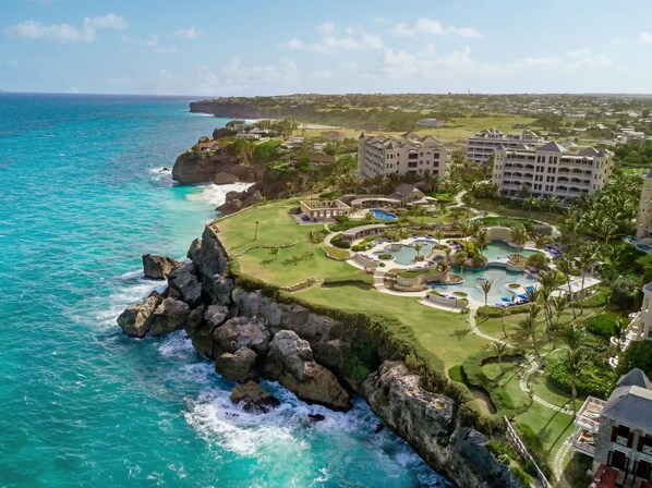 A coastal resort with a large pool area, multiple buildings, and a view of the ocean.