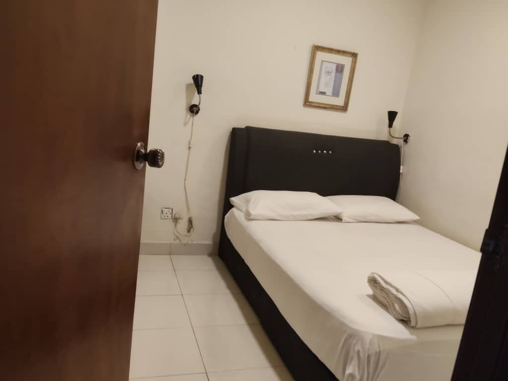 A hotel room with a bed, a door, a wall socket, and a framed picture.
