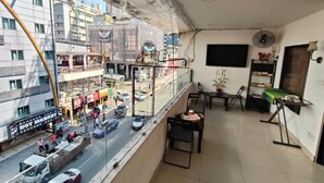 A balcony with a view of a busy street, a dining area with a table and chairs, and a wall-mounted TV. - NOVA HOTEL BUKIT BINTANG (Kuala Lumpur)