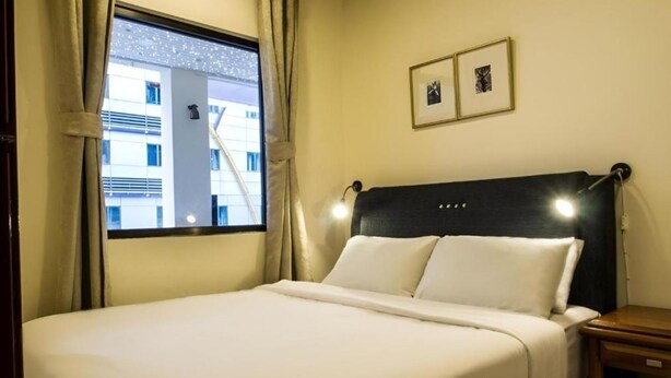 A hotel room with a bed, a nightstand, a window with curtains, and two framed pictures on the wall. - NOVA HOTEL BUKIT BINTANG (Kuala Lumpur)