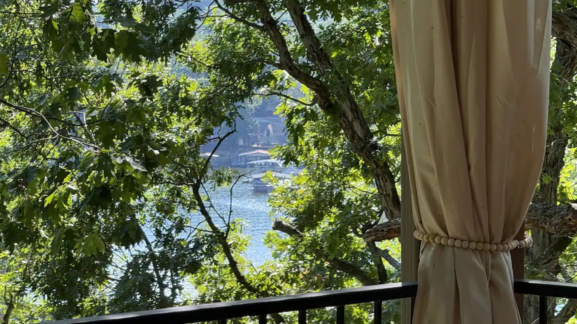 Vista desde un balcón con barandilla, sobre un cuerpo de agua y barcos, con árboles en primer plano.
