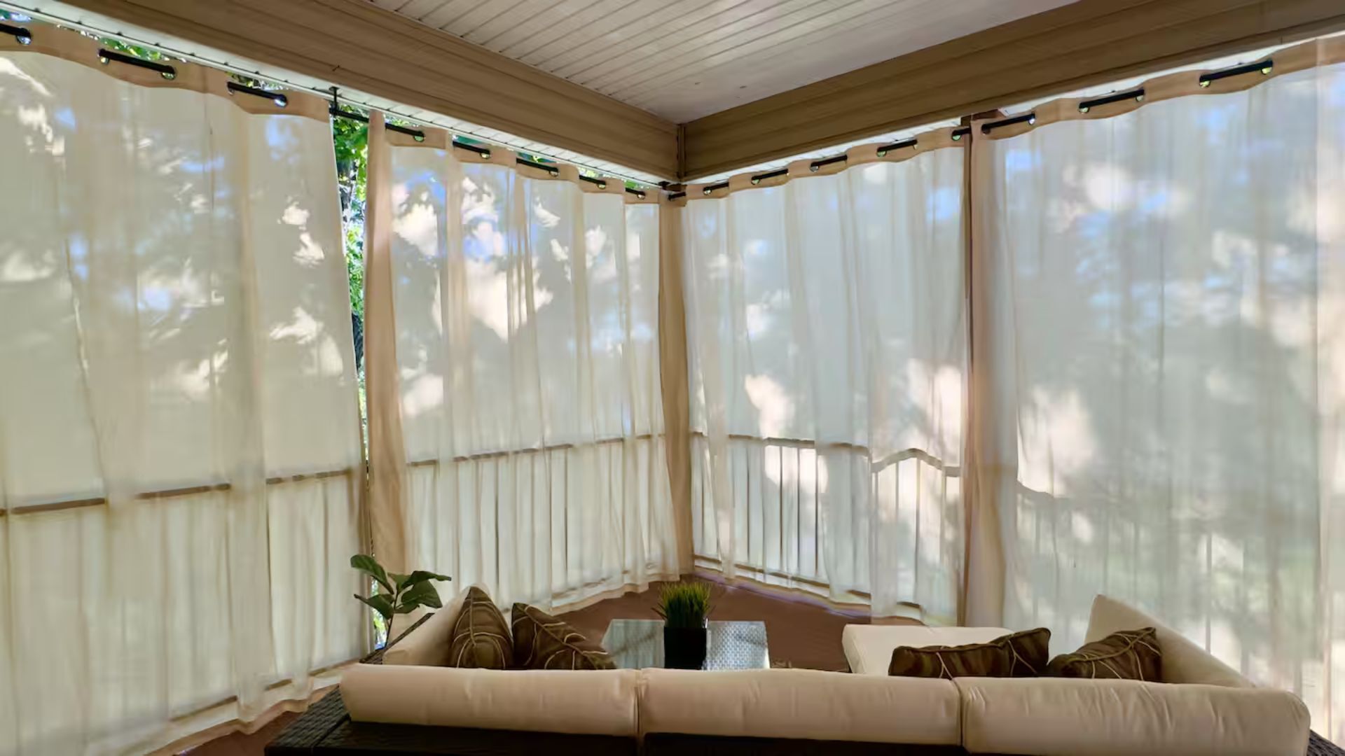 A sunroom with a beige sofa, a small table, and sheer curtains.