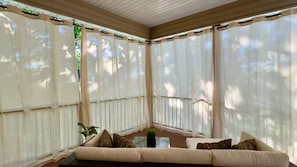 A sunroom with a beige sofa, a small table, and sheer curtains. - Lakeview HOUSE W/Hot Tub | 2 Units | 3 Bedrooms (Rocky Mount)