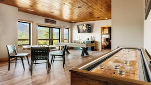 Una stanza con tavolo da biliardo, sedie, soffitto in legno e ampie finestre.