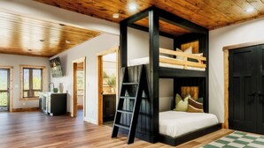Una stanza con un letto a castello, pavimento in legno, una scala, una porta nera e un tappeto a scacchi.