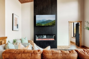 A living room with a fireplace, a mounted TV, and a view of mountains.