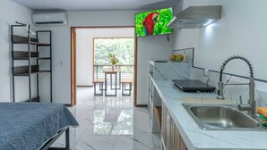 A compact hotel room with a bed, a kitchenette, a dining area with a table and chairs, and a large window providing a view of greenery. - Studio Apartment #7 w/ Smart TV, A/C + Pool (Playa negra)