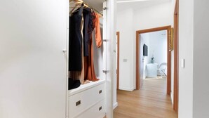 Een gang die leidt naar een slaapkamer met een kledingkast vol kleding.