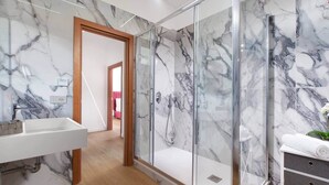 Een moderne badkamer met een marmeren spatwand, een douchecabine van glas en een houten vloer.
