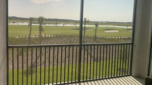 Vue depuis un balcon doté d’une rambarde en métal, donnant sur un terrain de golf avec des bunkers de sable et une étendue d’eau.