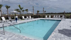 Une piscine rectangulaire, bordée d’une terrasse carrelée, entourée de chaises longues et de parasols, et offrant une vue sur le paysage environnant.