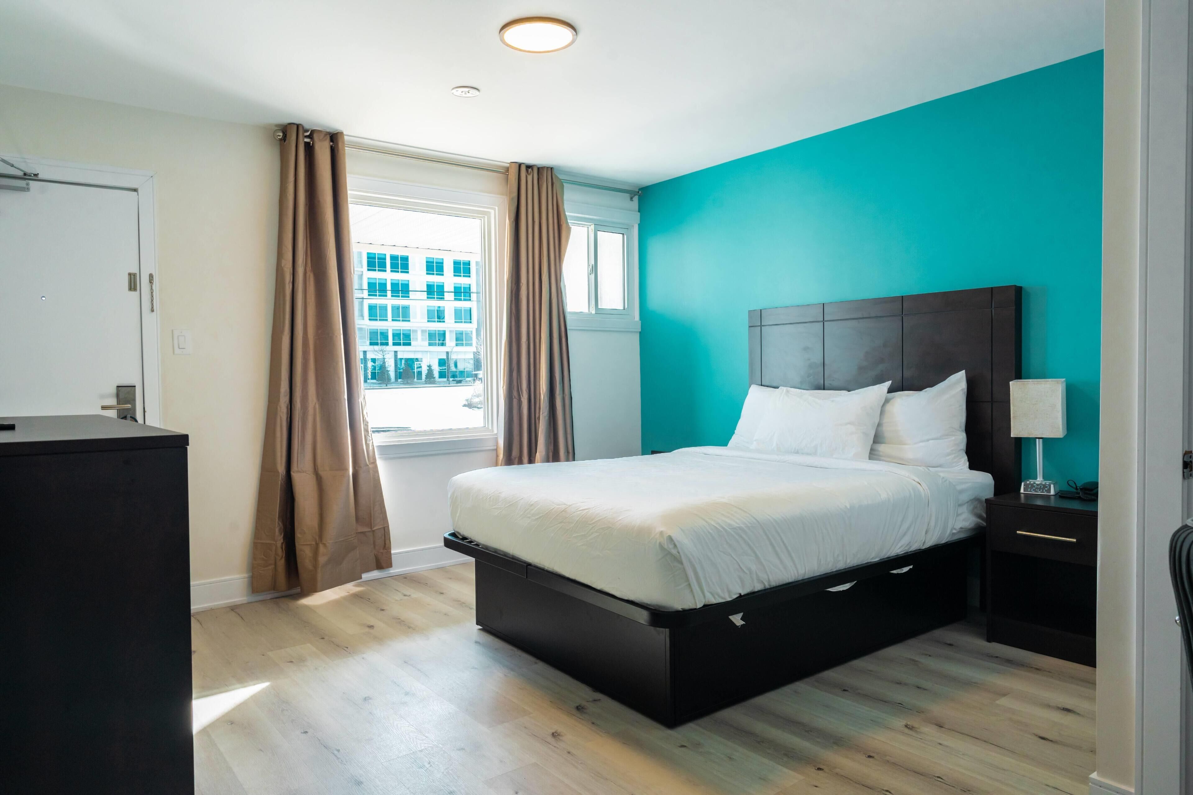 Un dormitorio con una cama, una mesita de noche, un escritorio y una ventana con cortinas.