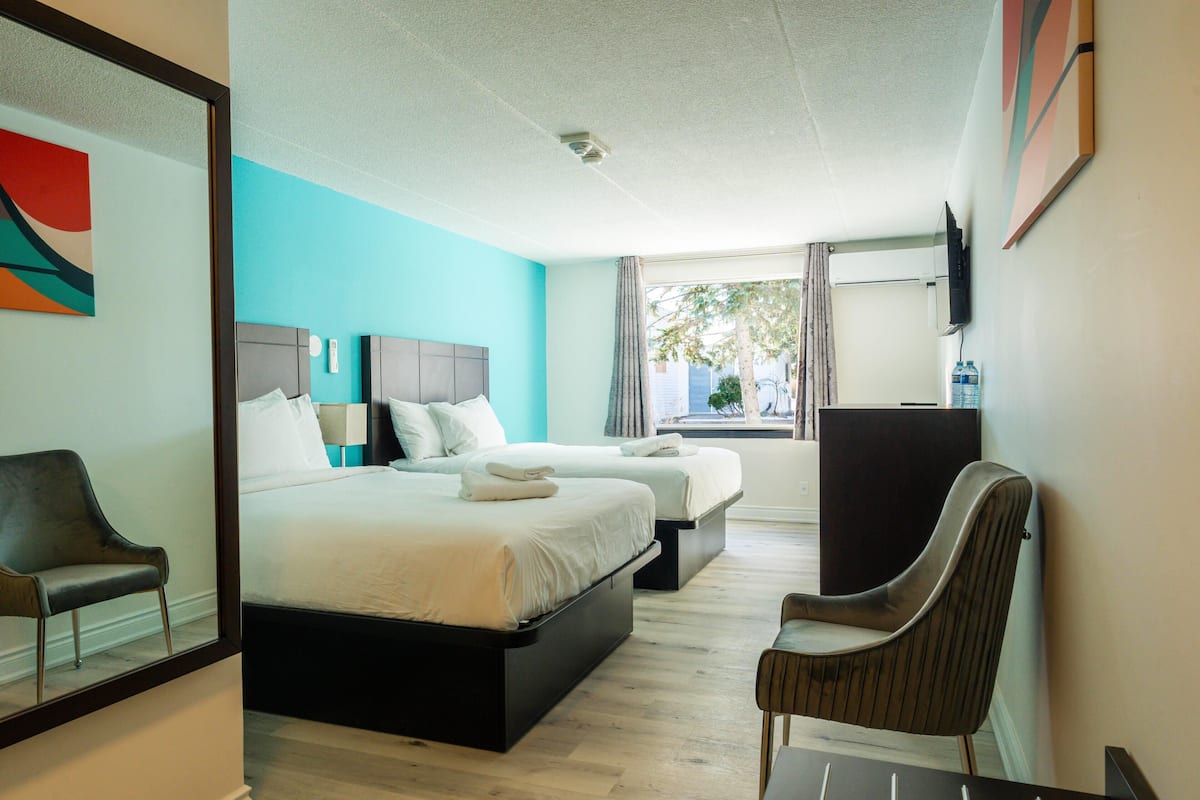 A hotel room with two beds, a chair, a TV, and a window with curtains.