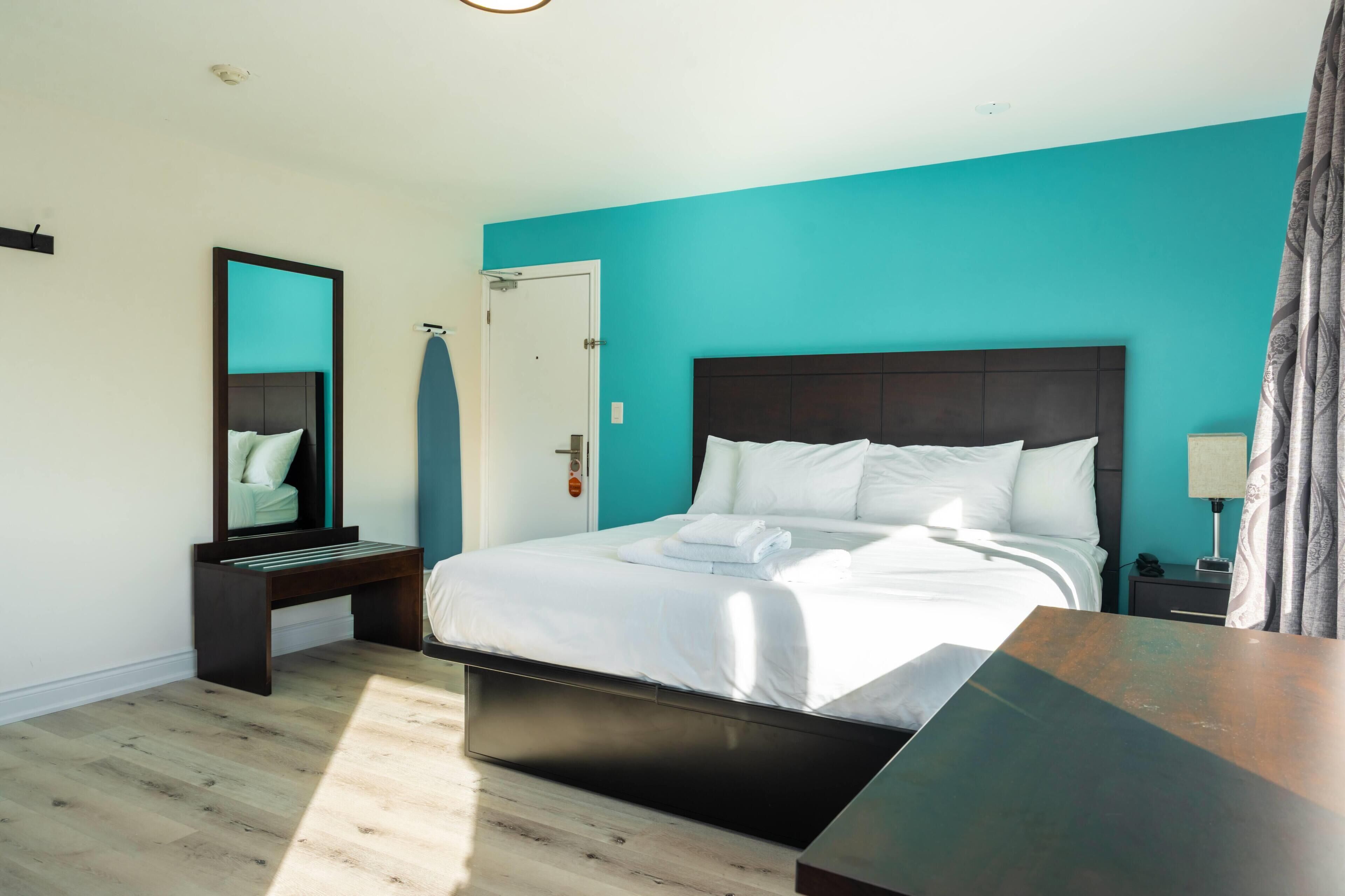 A modern hotel room with a large bed, a bedside table, a nightstand, a mirror, and a door.