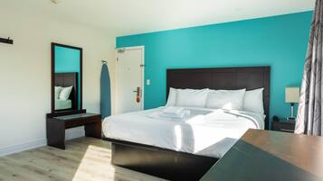 A modern hotel room with a large bed, a bedside table, a nightstand, a mirror, and a door.