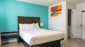Une chambre à coucher comprenant un lit, une table de chevet, une lampe fixée au mur et une porte donnant sur une salle de bain.